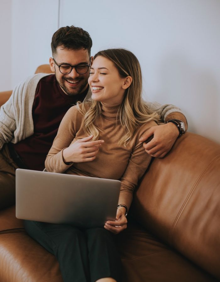 Couple sitting in their Minneapolis apartment on brown leather couch smiling